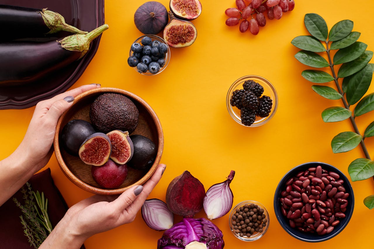 Colorful arrangement of fruits and vegetables on a yellow background, featuring figs and eggplants.